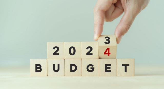 Claves para realiza el seguimiento presupuestario de la empresa 7 claves para realizar un seguimiento efectivo de tus presupuestos anuales. Imagen de una mano volteando un cubo de madera cambiando el 2023 por el 2024