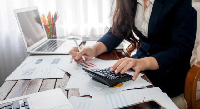La contabilidad como primera línea de defensa ante comprobaciones y sanciones tributarias. Imagen de una mujer empresaria haciendo cuentas en su mesa de ordenadro con sus gráficos