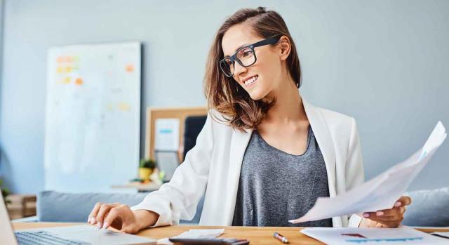 Contable. Mujer trabajando sonriente con su portátil y unos documentos