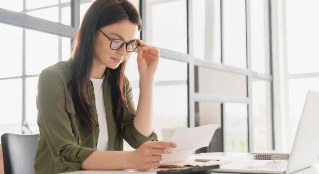 ¿Cuál es el tratamiento contable y fiscal de la compensación de facturas o netting? Imagen de una chica joven mirando un papel con su portatil en la mesa